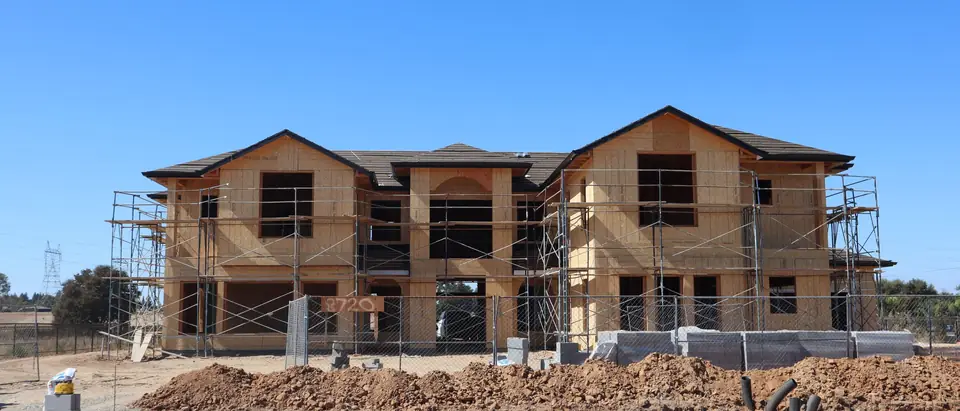 A new two-story house in its wood frame, wrapped in scaffolding under a blue sky