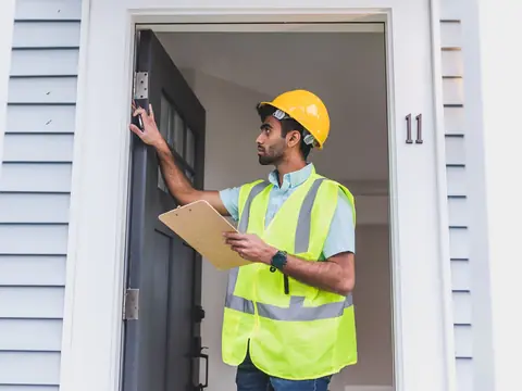 A builder in a hi-vis vest and hard hat checking a front door