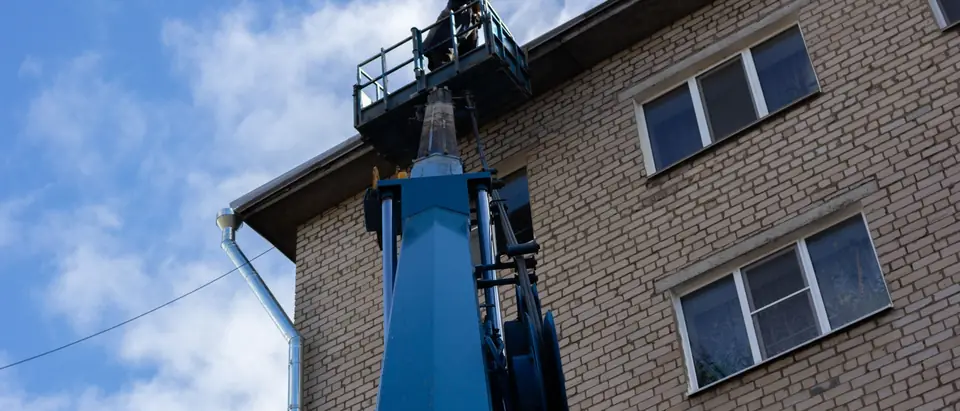 A boom lift against a brick building under a blue sky