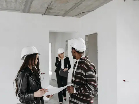 Three people in hard hats walking through a new building with drawings