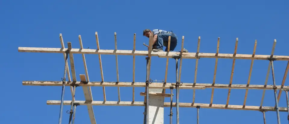 A builder on a scaffold frame high against a deep blue sky