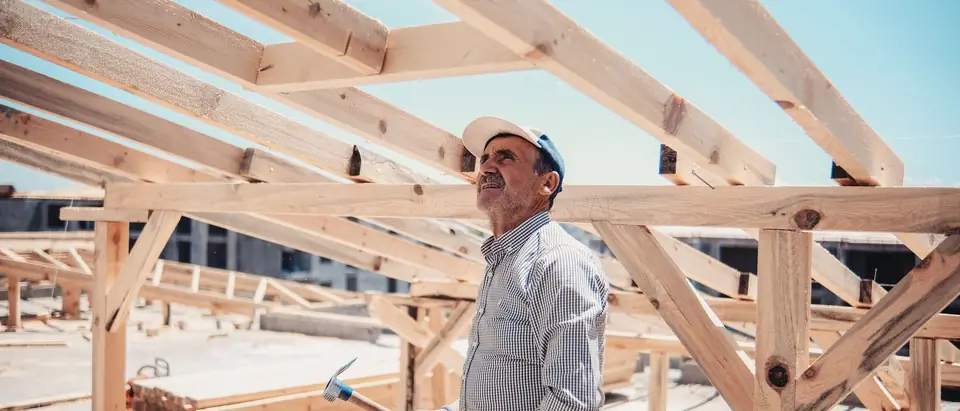 A builder looking up at a new timber frame under a blue sky