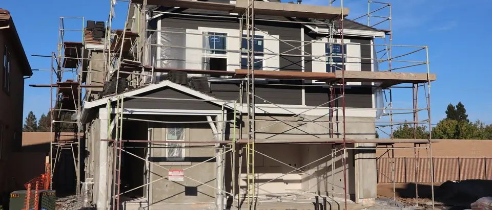 A two-story house under construction in scaffolding on a sunny day