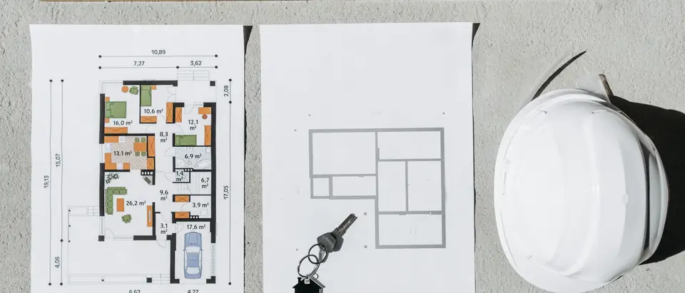 House plans, a spirit level and a white hard hat laid out on a table