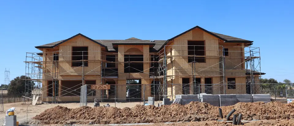 A large two-story home in its wood frame, ringed by scaffolding