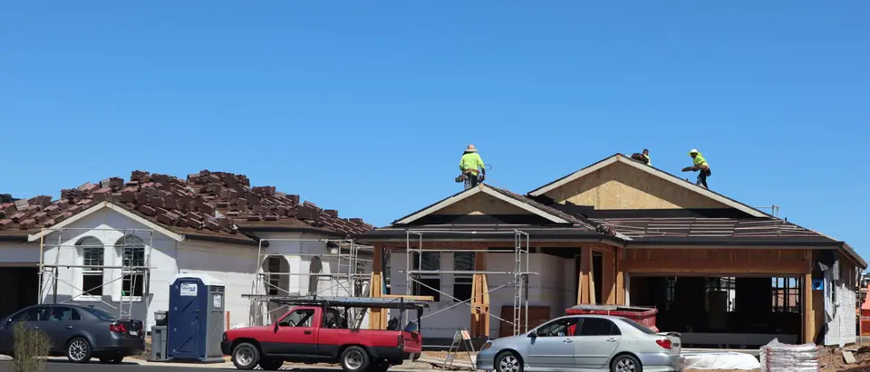 Roofers on new suburban homes under a clear blue sky