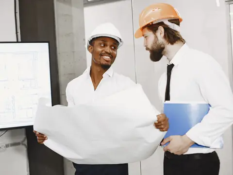 Two men in hard hats going over a large drawing in an office
