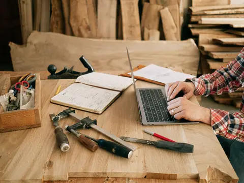 A laptop, notebook and hand tools on a woodworker's bench