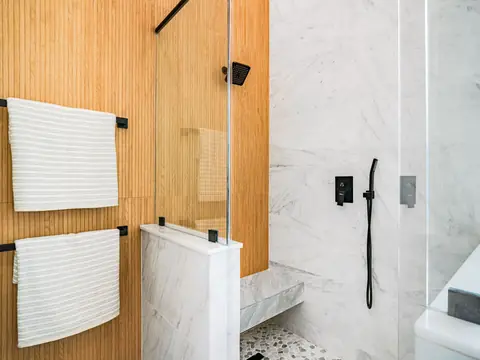 A finished bathroom with marble tile, wood paneling and a glass shower
