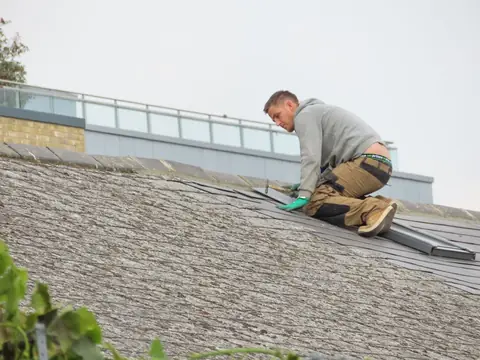 A roofer laying shingles on a pitched roof