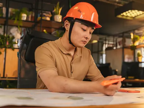 A man in an orange hard hat working through drawings at a desk